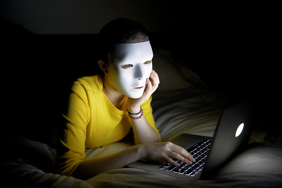 Anonymous teenager in mask on internet at night Photograph by Peter Dazeley