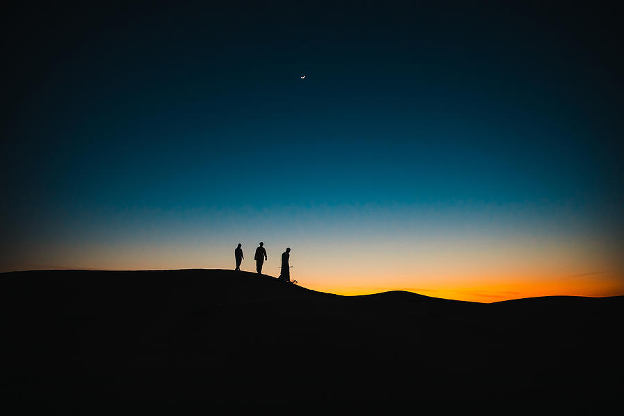 Arabs on the sand dunes walking behind each other during twilight Photograph by GCShutter