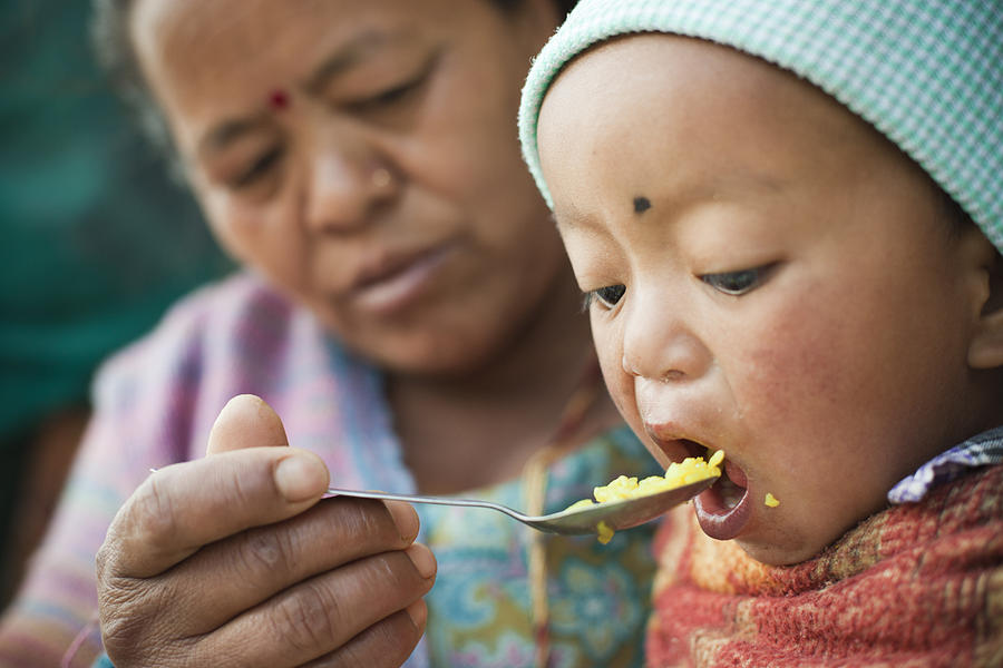 Asian woman feeding food to little child. Photograph by Gawrav Sinha