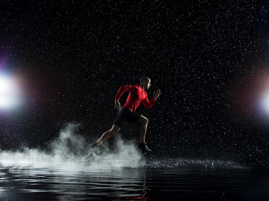 Athlete running in rain through water at night Photograph by Jonathan Knowles