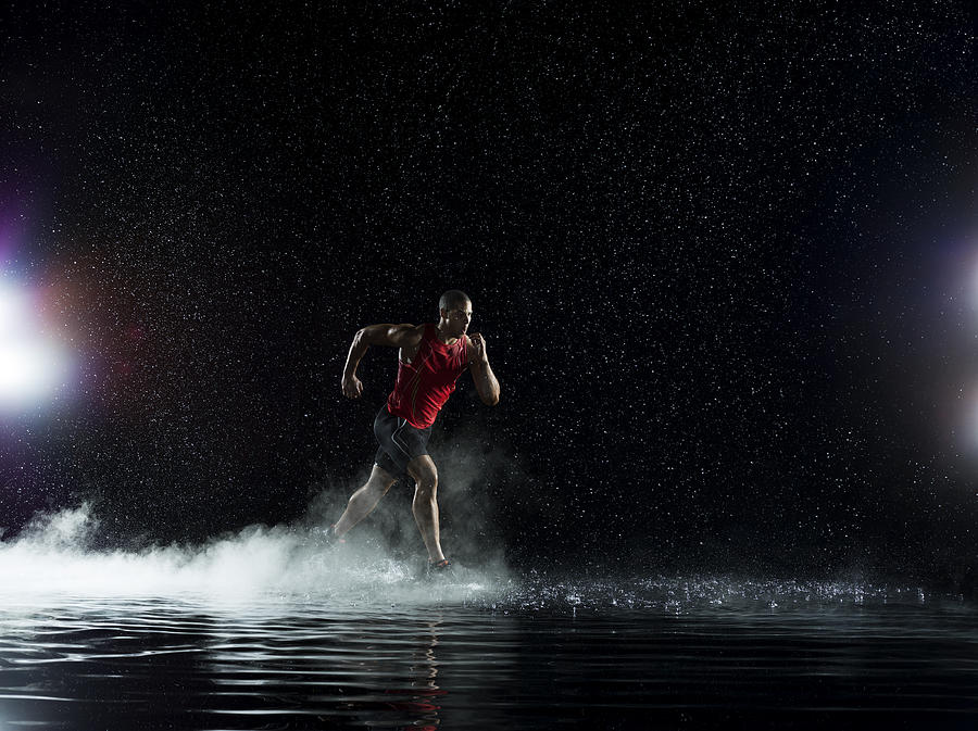 Athlete running in water in rain at night Photograph by Jonathan Knowles