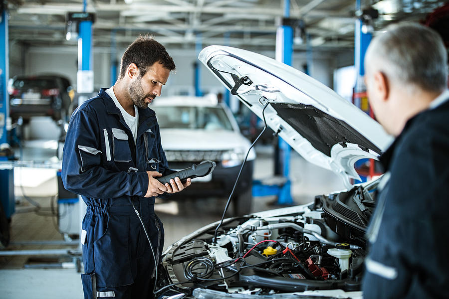 Auto mechanic working with car diagnostic tool in a repair shop. Photograph by Skynesher