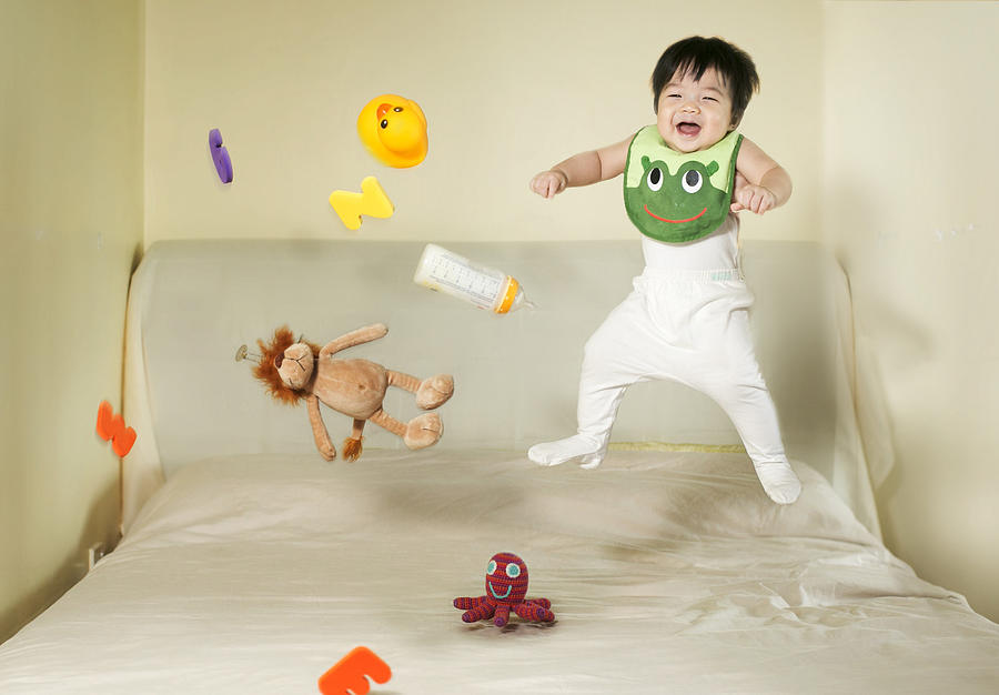 Baby boy and toys jumping on bed. Photograph by Twomeows