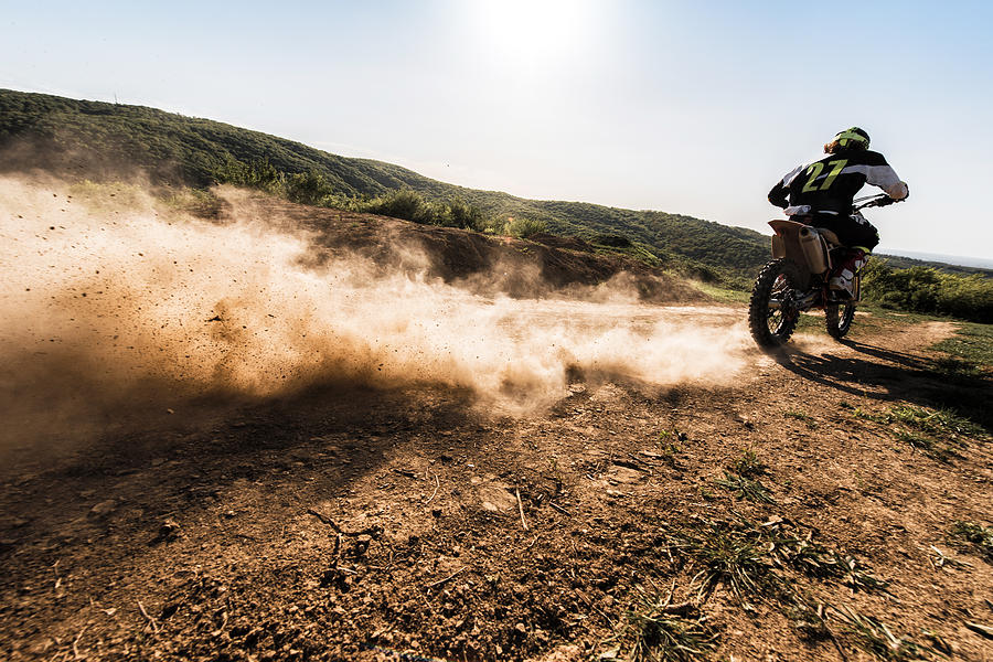 Back view of motocross rider driving fast on dirt track. Photograph by Skynesher