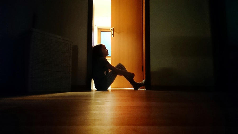 Backlit child sitting in a dark doorway in contemplation Photograph by Elva Etienne