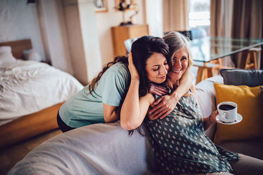 Beautiful adult daughter embracing smiling senior mother sitting on sofa Photograph by Wundervisuals