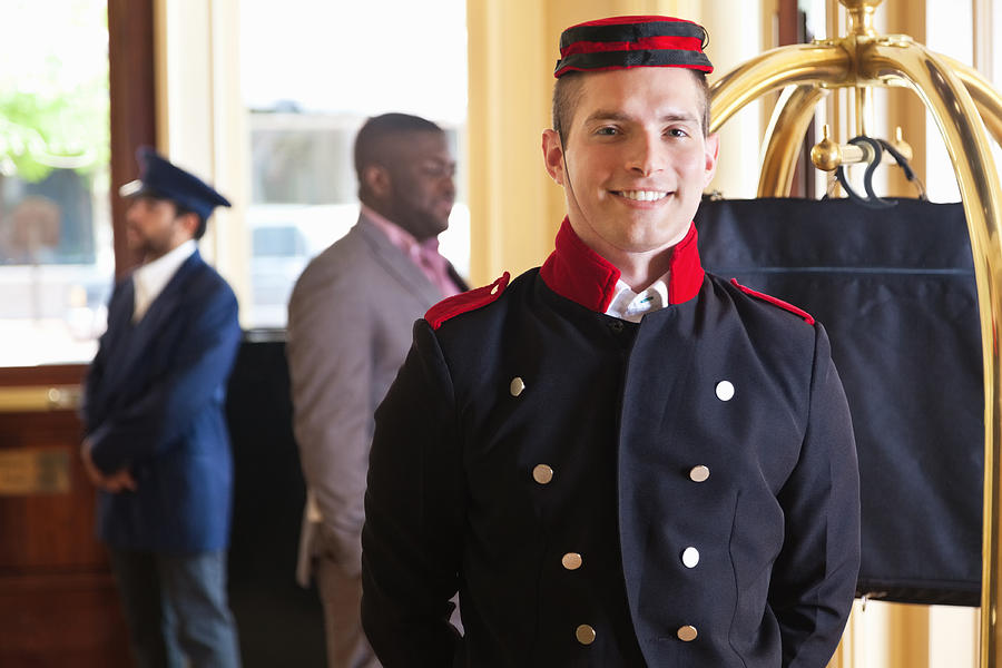 Bellhop standing in hotel lobby with guests luggage on cart Photograph by SDI Productions