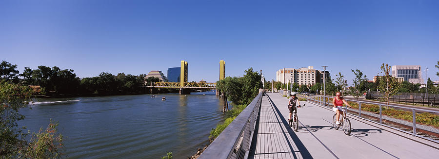 Architecture Photograph - Bicyclists Along The Sacramento River by Panoramic Images