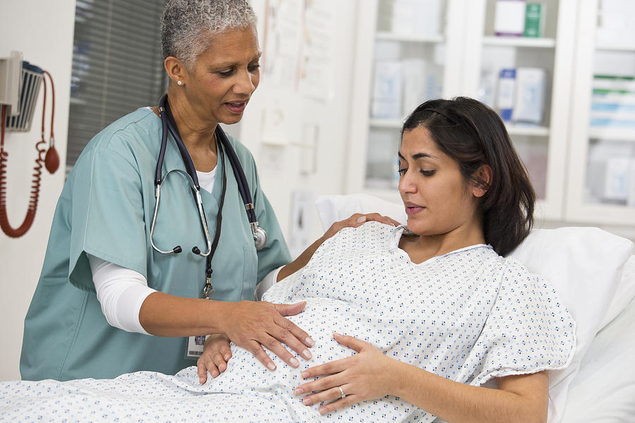 Black doctor examining pregnant patients belly Photograph by Ariel Skelley