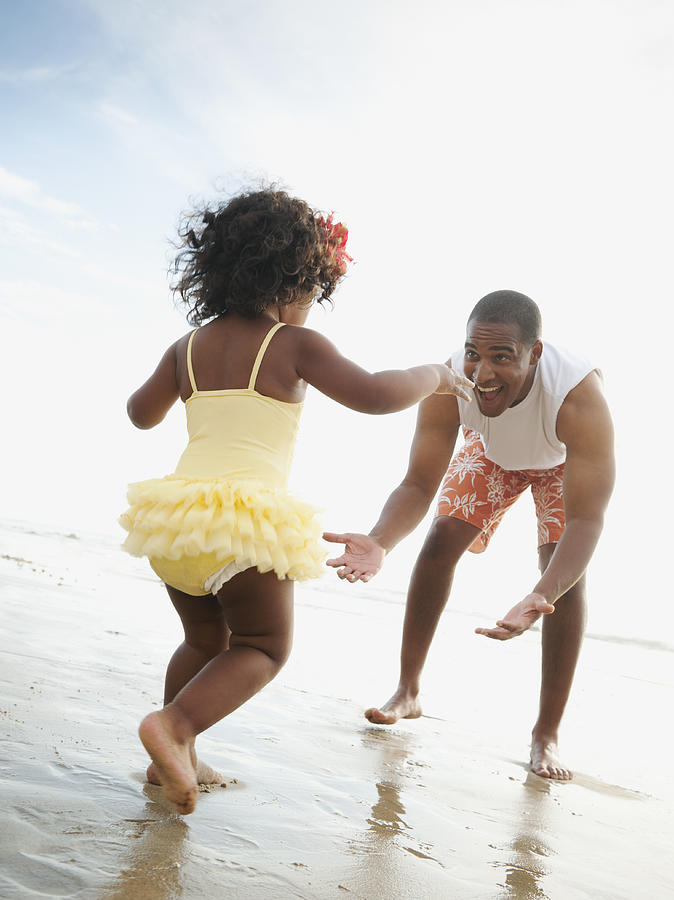 Black father bending to greet daughter on beach Photograph by Blend Images - Erik Isakson