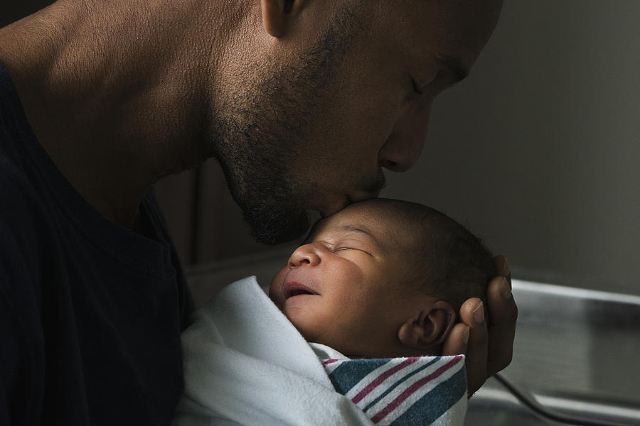 Black father kissing forehead of newborn son Photograph by Ariel Skelley