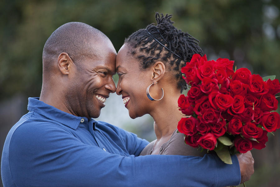 Black man hugging wife and giving her red roses Photograph by Ariel Skelley