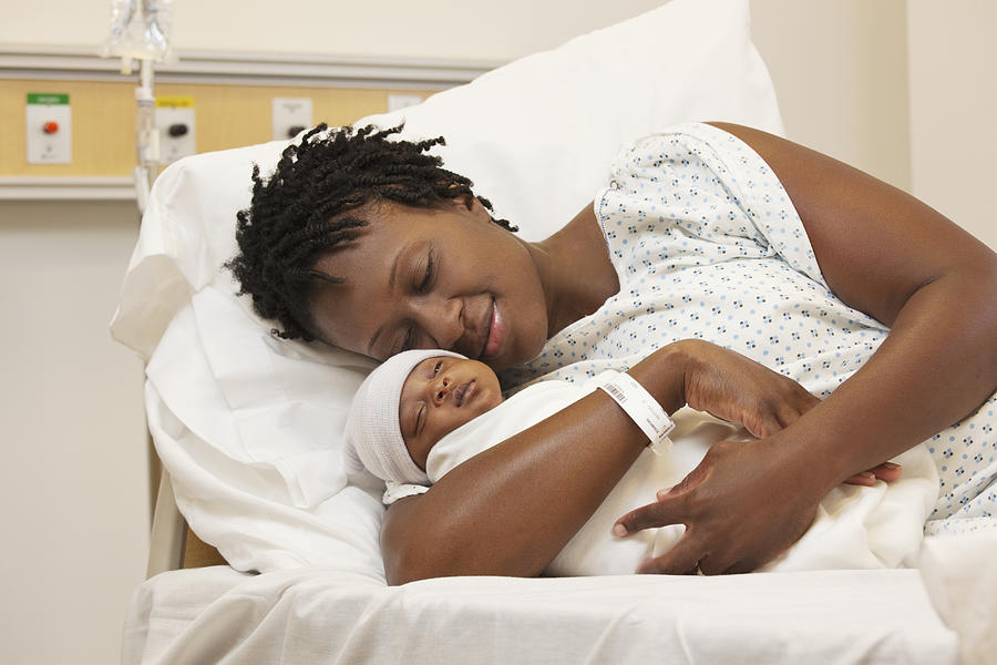 Black woman holding newborn baby in hospital bed Photograph by Ariel Skelley
