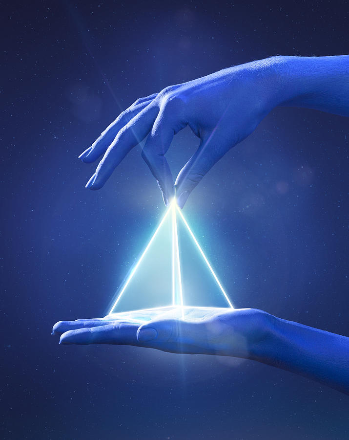 Blue painted hand pinching a glowing light prism Photograph by Paper Boat Creative