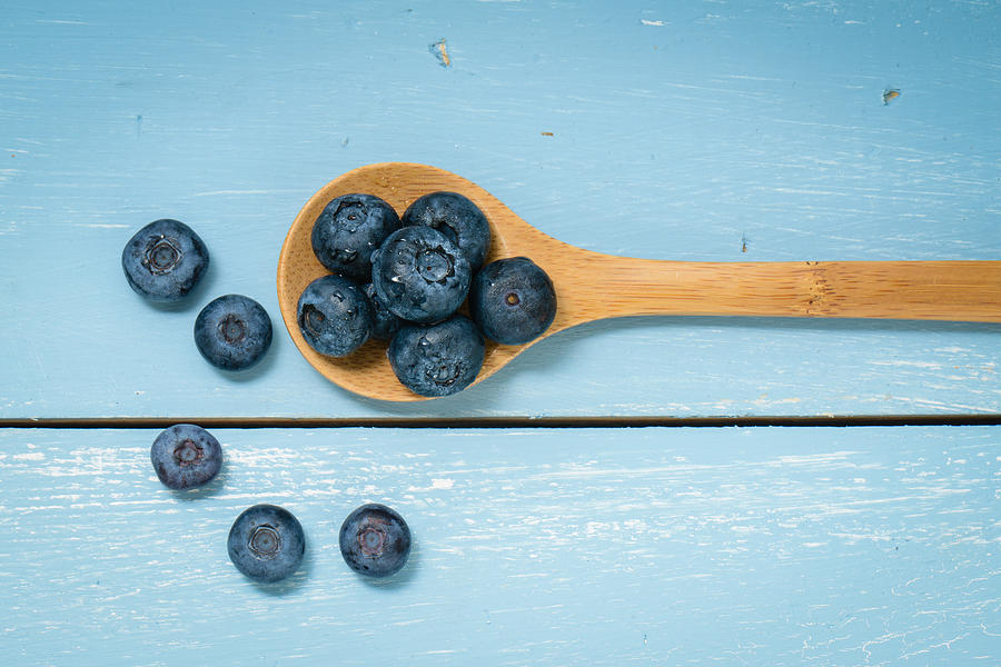 Blueberries on a Spoon lying on Blue Wood Background Photograph by Brandon Bourdages