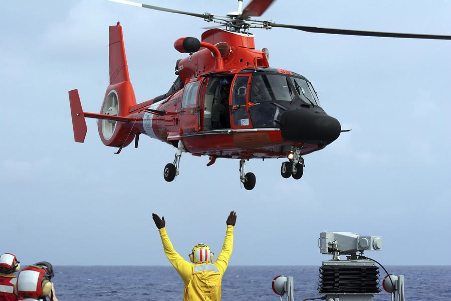 Boatswain Mate directs a HH-65A Dolphin aboard the guided-missile destroyer USS Russell. Photograph by Stocktrek Images