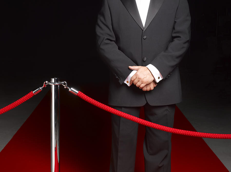 Bouncer security man standing on red carpet by ropes, mid section Photograph by Peter Dazeley