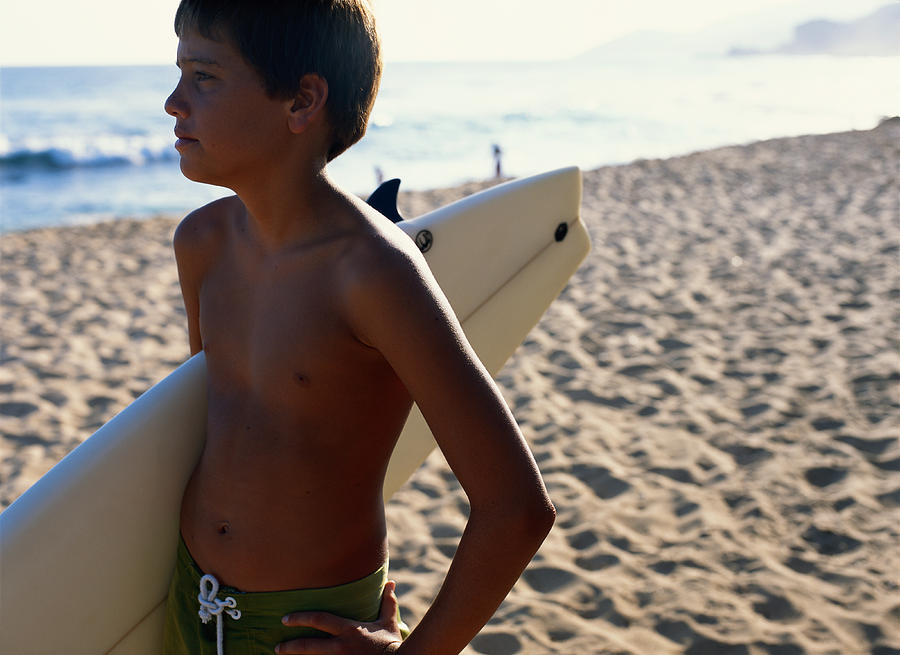 Boy (11-12) with surfboard standing at beach, looking away Photograph by Hitoshi Nishimura