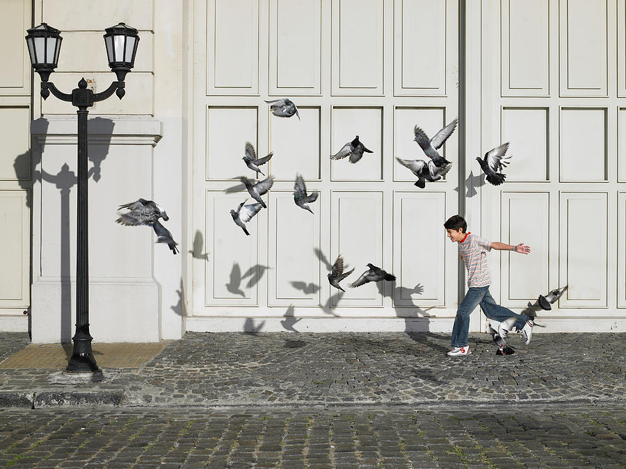 Boy (11-13) chasing pigeons in street Photograph by Michael Blann