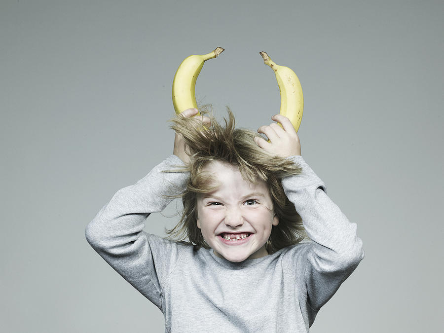 Boy (6-7) holding two banana on head, smiling, close-up Photograph by Flashpop