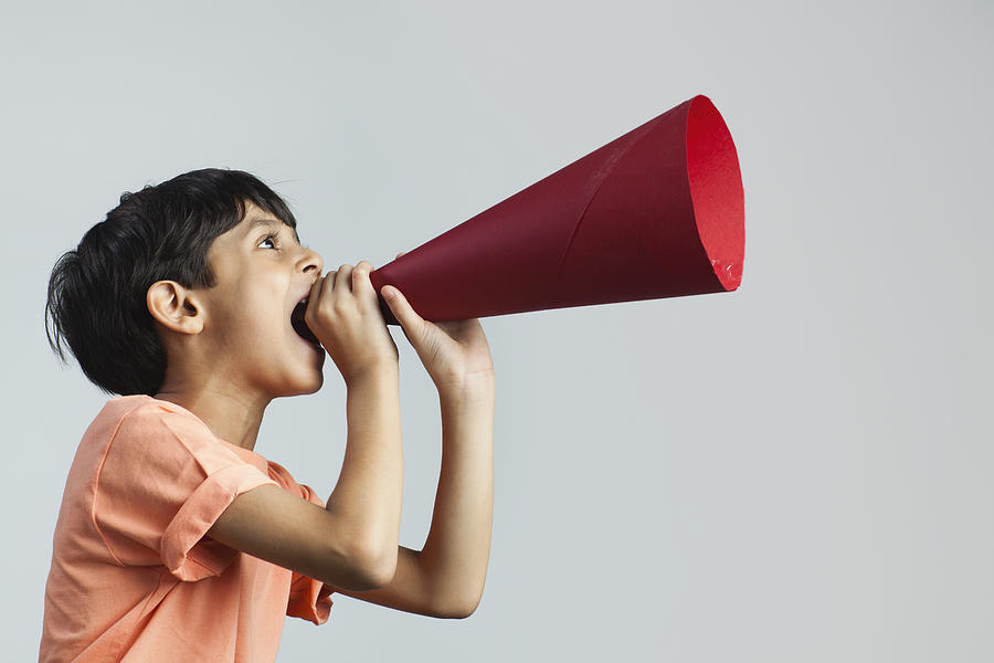 Boy (6-7) shouting through paper megaphone Photograph by ImagesBazaar