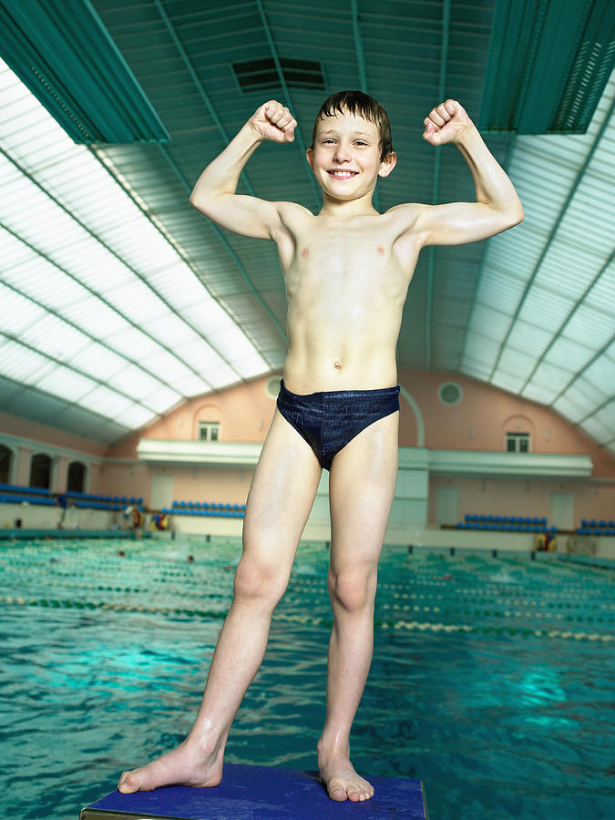 Boy (8-9) flexing muscles at swimming pool, smiling, portrait Photograph by Hans Neleman