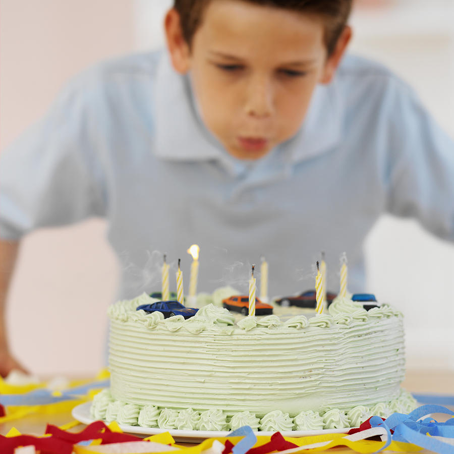 Boy (9-10) blowing out candles on a birthday cake Photograph by Stockbyte