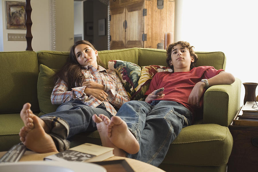 Boy and girl sitting on sofa with remote control Photograph by Jupiterimages