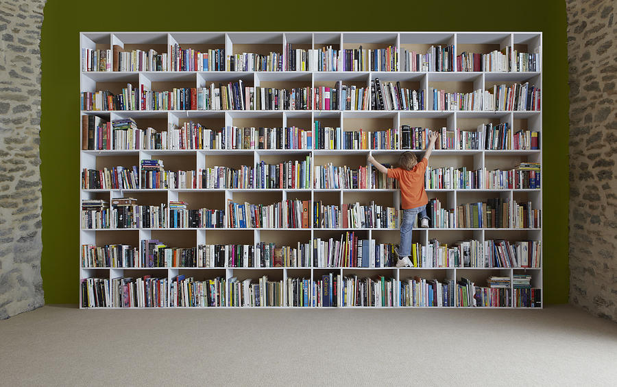 Boy climbing bookshelves Photograph by Tim Macpherson