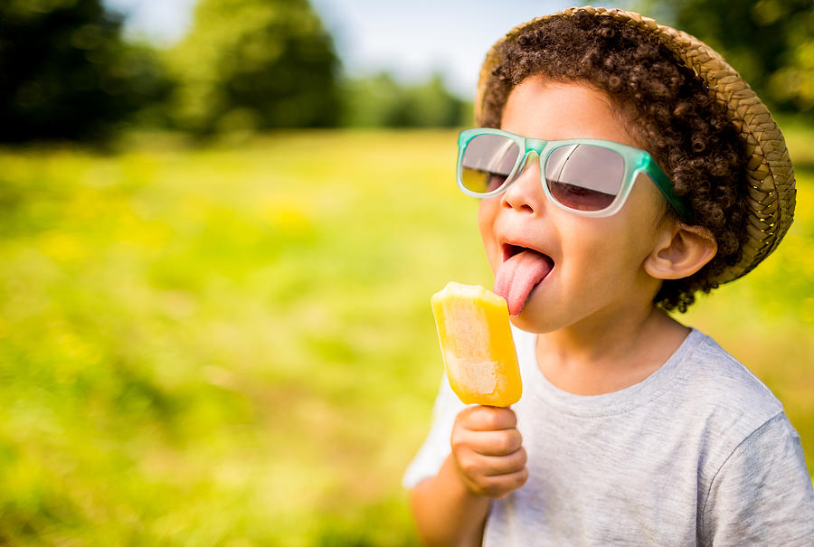 Boy in sunglasses and hat eating popsicle outdoors Photograph by Wundervisuals