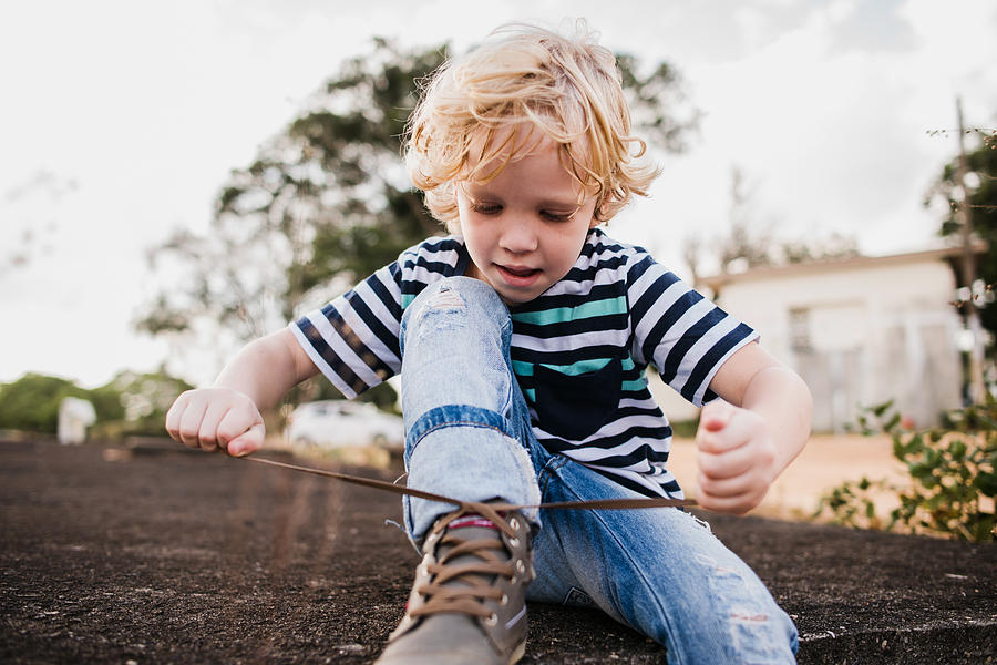 Boy learning to tie his shoelaces Photograph by Camilla Bandeira