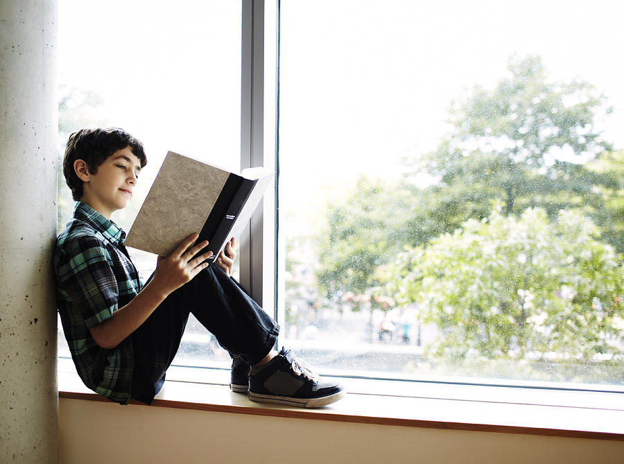 Boy reading book sitting in window nook Photograph by Andy Ryan