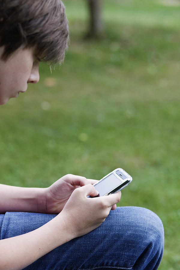 Boy texting on PDA Photograph by Compassionate Eye Foundation/Jetta Productions