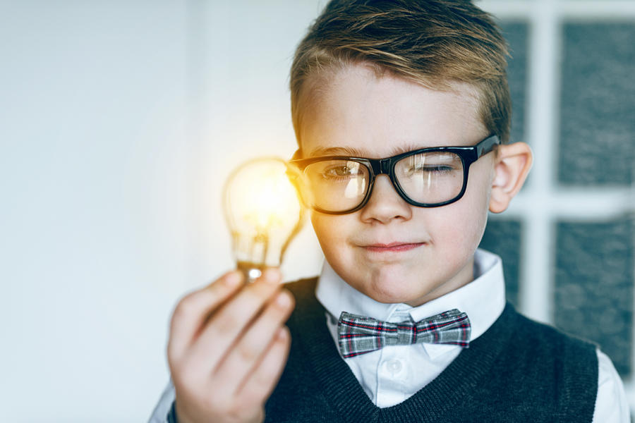 Boy with glasses and bow tie looks at glowing light bulb and gets an idea Photograph by Mikkelwilliam