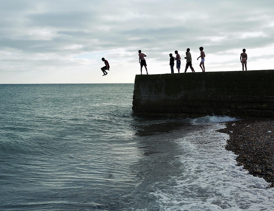 Boys Jumping Off A Pier On The Seafront Photograph by Fiona Crawford Watson