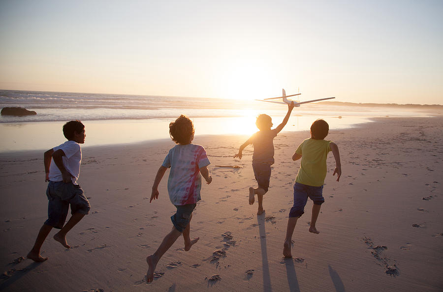 Boys running along beach with a toy plane Photograph by Alistair Berg