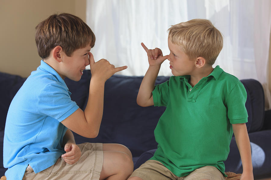 Boys with hearing impairments signing silly in American sign language on their couch Photograph by Huntstock