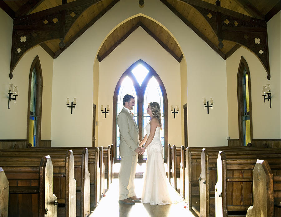 Bride and groom holding hands in chapel, side view Photograph by Dana Neely