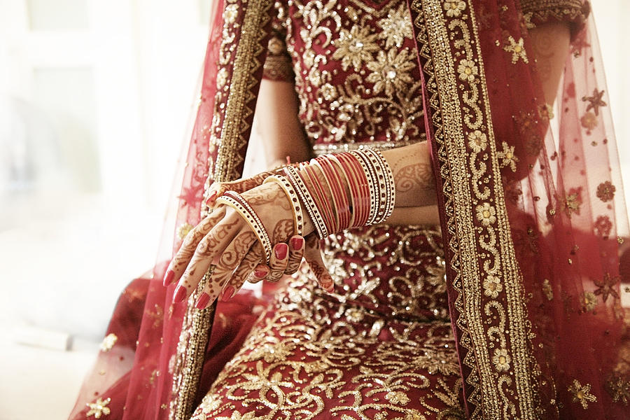 Bride putting on her red glass bracelets Photograph by Paper Boat Creative