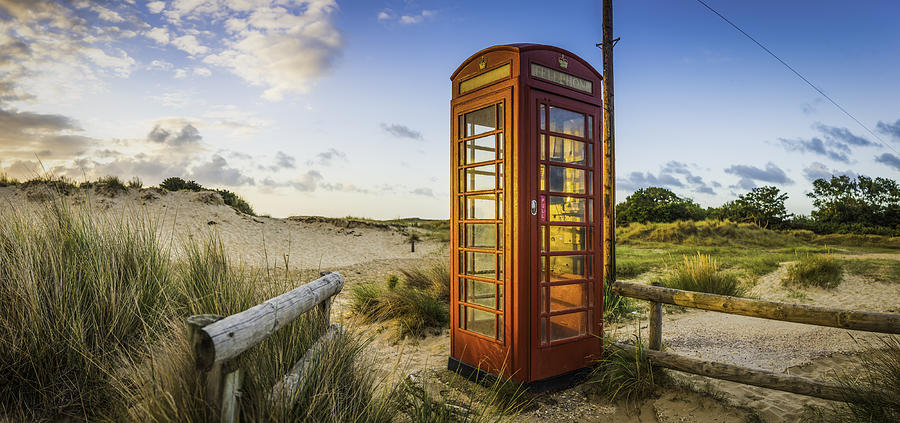 British red telephone box illuminated at sunrise on seaside beach Photograph by fotoVoyager