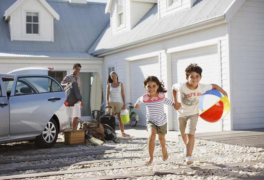 Brother and sister with beach ball running on driveway Photograph by Tom Merton