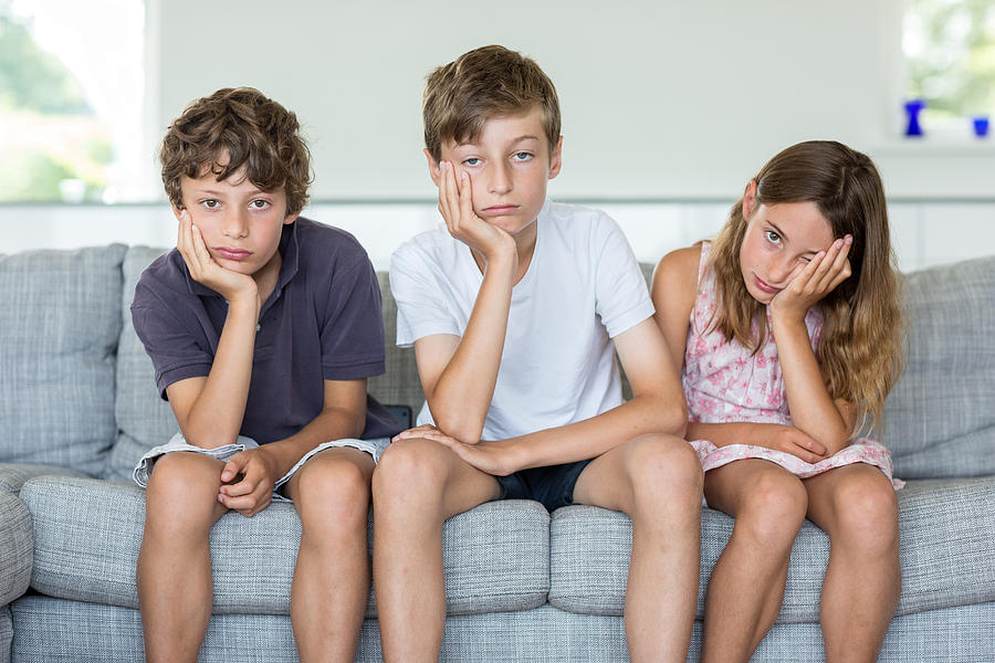 Brothers and sister on sofa looking bored Photograph by Richard Lewisohn
