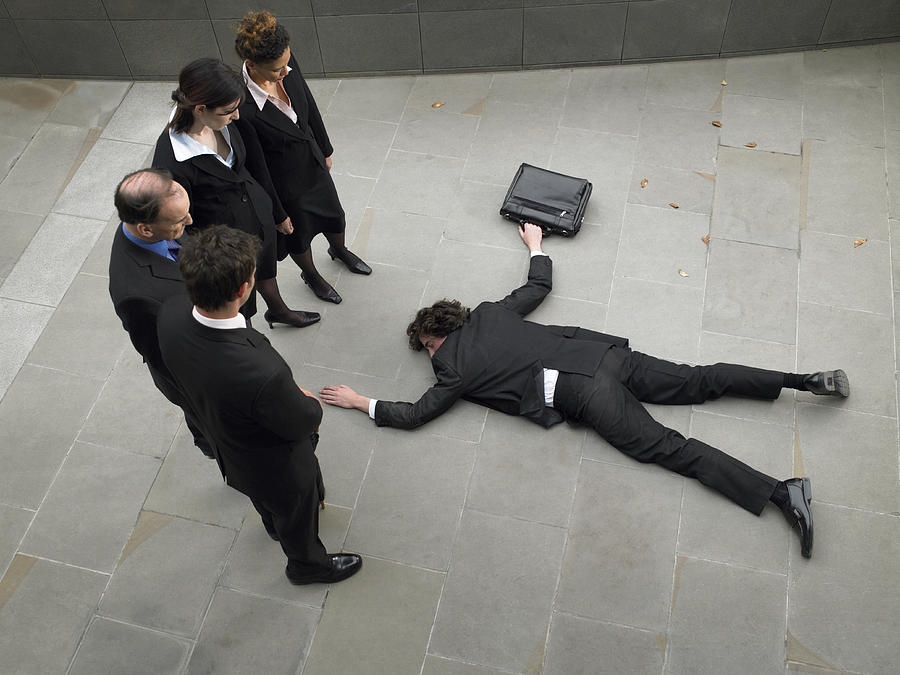 Business people looking down at man lying on pavement, elevated view Photograph by Michael Blann