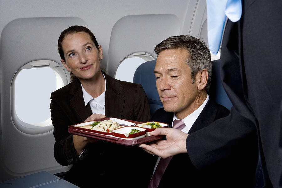 Business people on a plane being served airline food Photograph by Halfdark