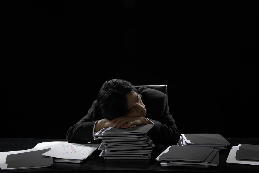 Businessman asleep at desk resting head on stack of files Photograph by James Woodson