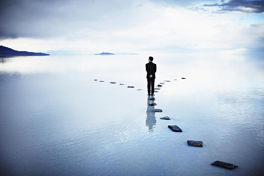 Businessman at fork of stone pathway in water Photograph by Thomas Barwick