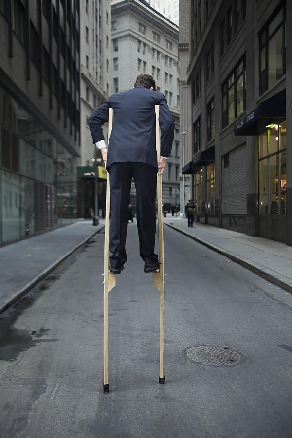 Businessman balancing on stilts Photograph by Sean De Burca