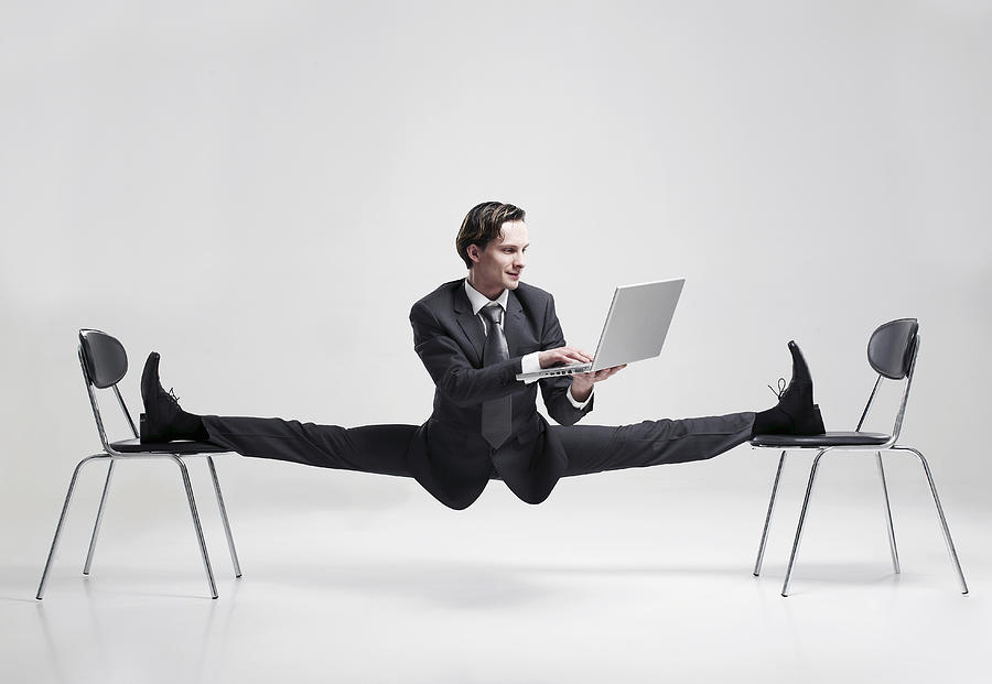 Businessman balancing to two chairs holding laptop Photograph by Mike Harrington