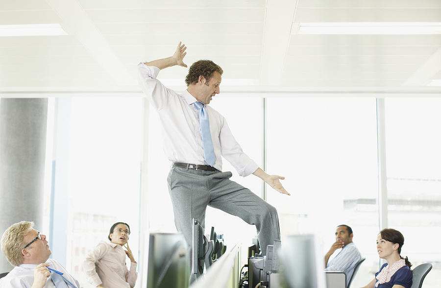 Businessman dancing on desk in cubicle Photograph by Paul Bradbury
