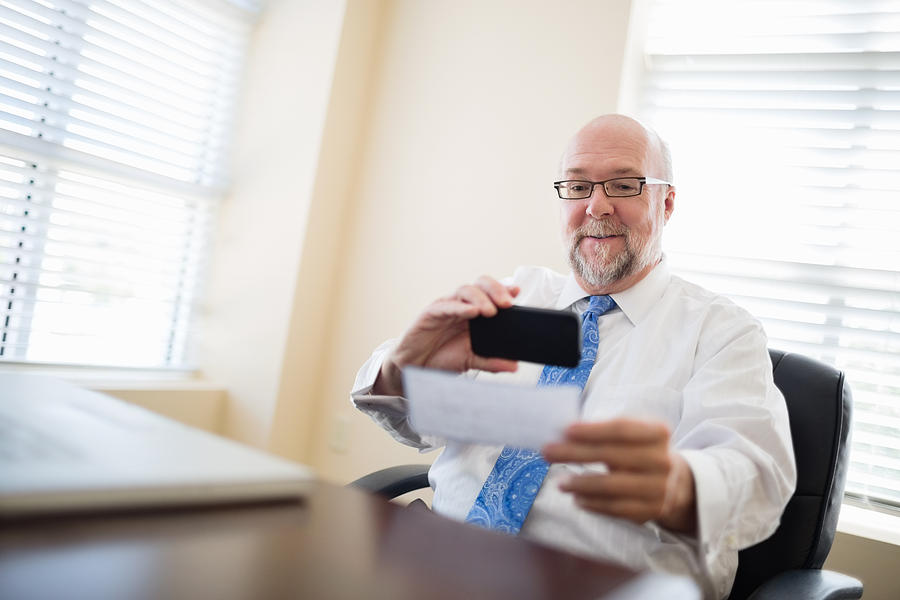 Businessman depositing check via smartphone from his office Photograph by PhotoInc